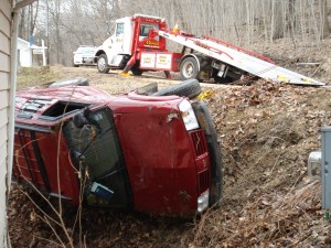 Photo of a light duty tow truck receiving and towing a vehicle in the ditch.